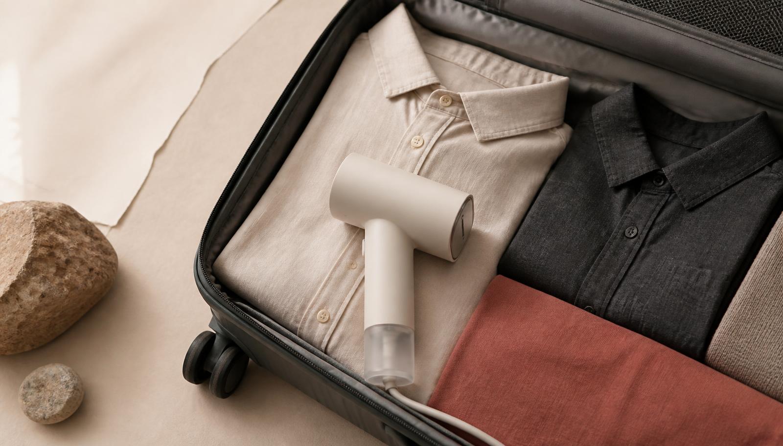 A small handheld steamer packed in a carry-on suitcase with folded shirts