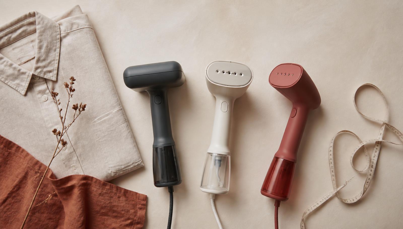 Three handheld travel steamers laid out beside a folded shirt and a measuring tape